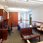 Admin office with red wooden color executive and computer desk with a black leather chair and multicolored pattern floor.