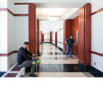 Two men in a large white hallway with redwood pillars and marble checkered floors.