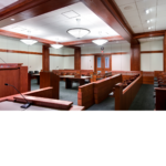 View of the courtroom from the witness stand facing a podium and jury bench. 