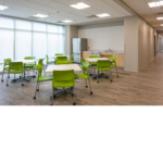 Employee eating room with four tables and green chairs.