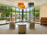 A conversation area with four green floral print seats surrounding a coffee table in the corner of a glass wall.