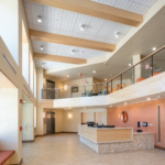 High ceiling front entrance with a reception desk to the left and light brown flooring and a visible 2nd floor.