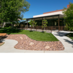 The exterior walkway of the La Vida Llena building with a view of xeriscaped lawn with grass.