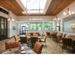 A natural-lit dining hall with floral seats and silverware neatly placed on tables.