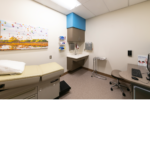 Exam room with an exam table and a white sink and grey desk.