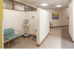 Triage cubicle with a teal chair and blood pressure monitor on stand by. 